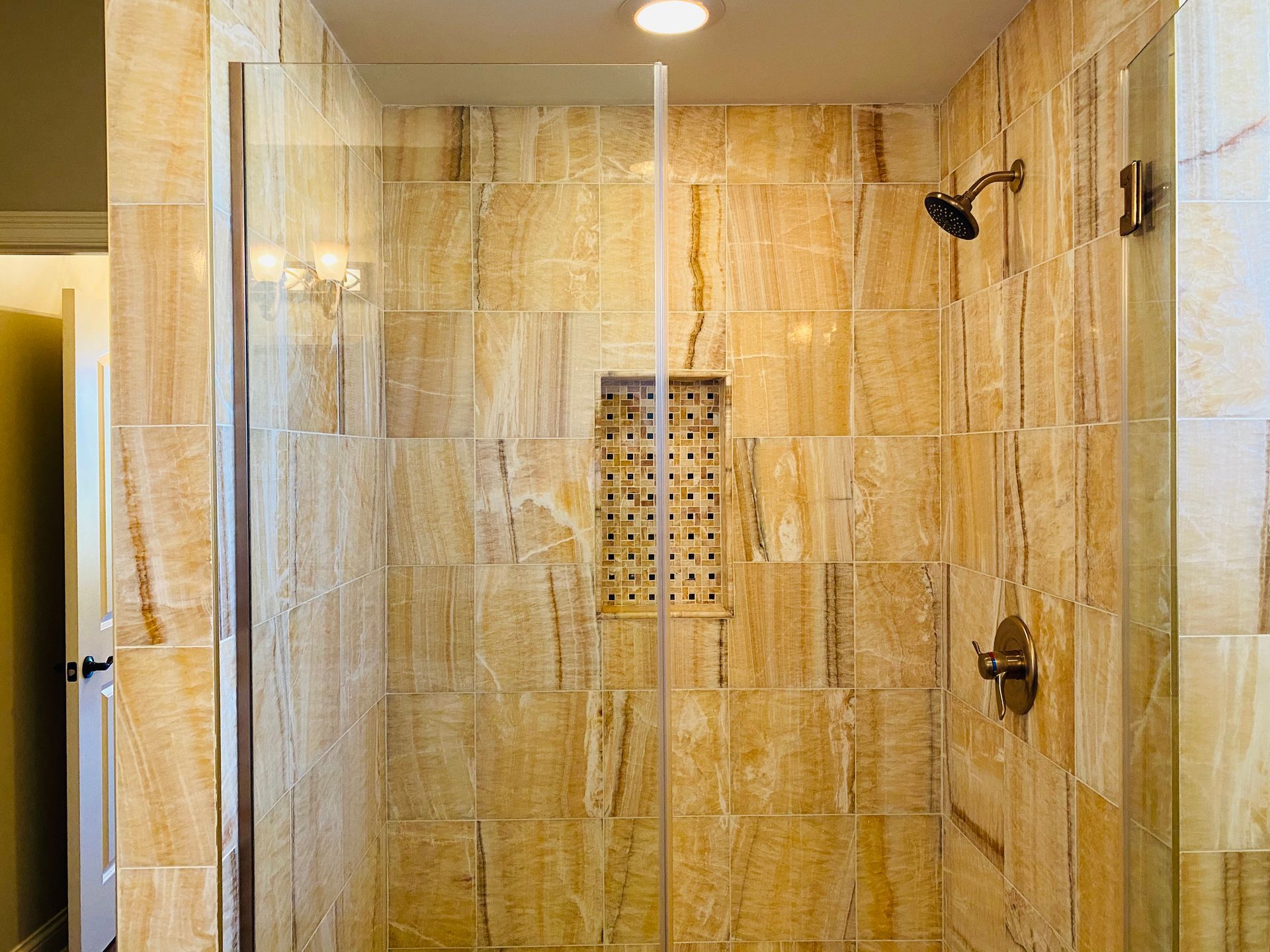 A bathroom with a walk in shower with a glass door and tiled walls.