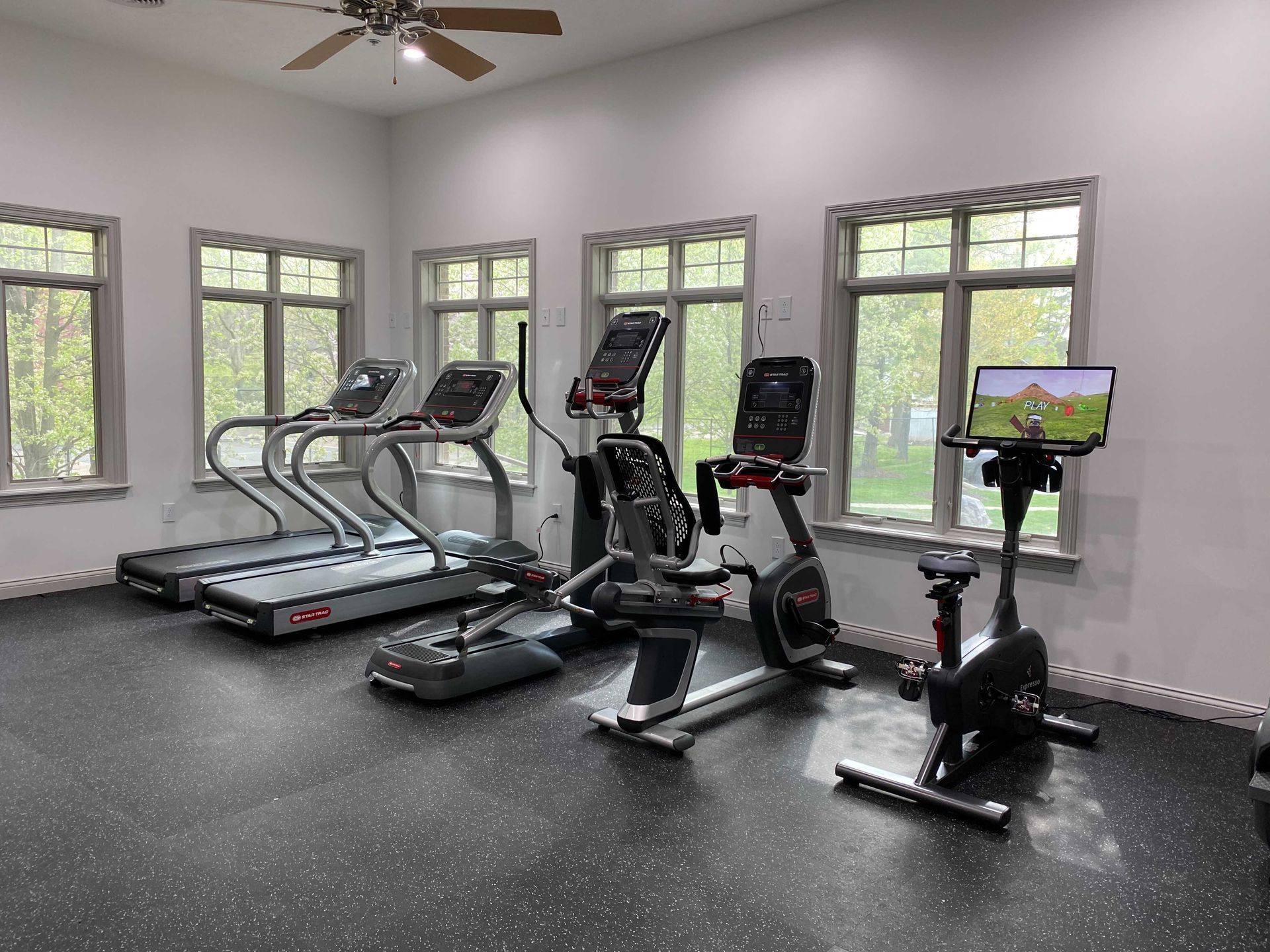 A gym with treadmills , exercise bikes , and a ceiling fan.