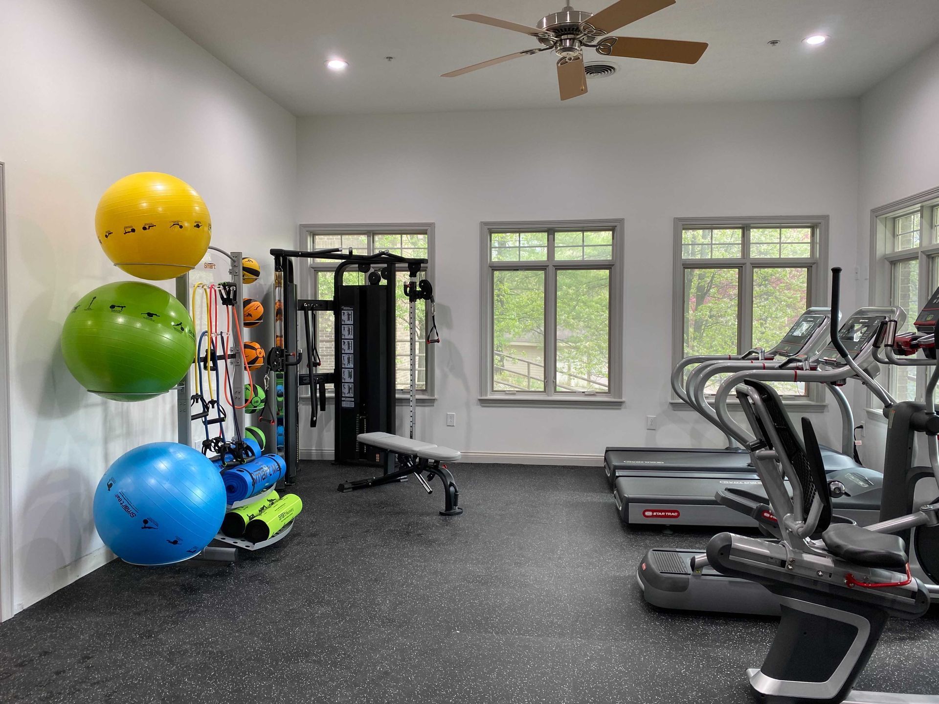 A gym with a lot of exercise equipment and a ceiling fan.