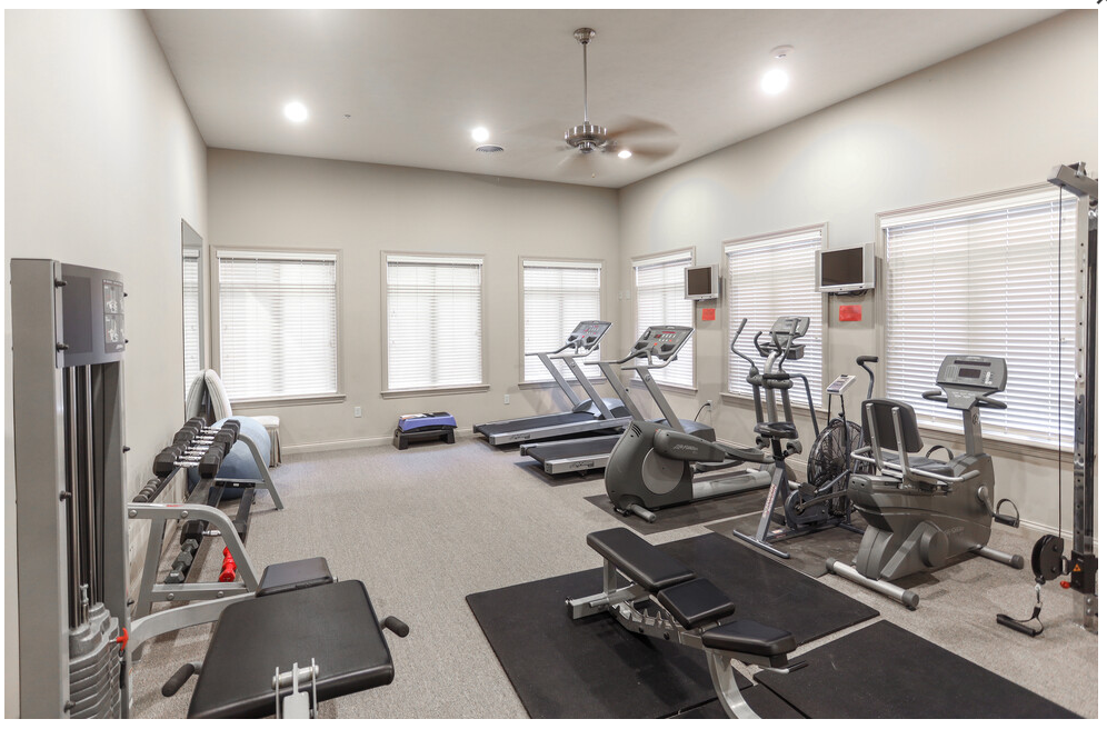 A large gym with a lot of equipment and a ceiling fan.