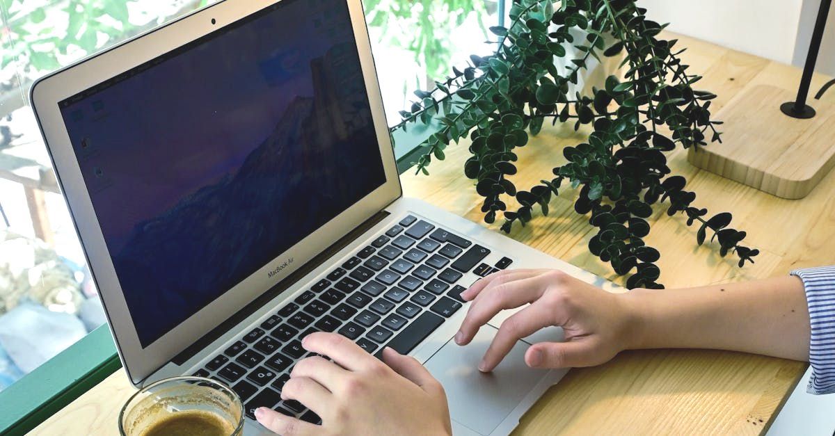 A person is typing on a laptop computer next to a cup of coffee.