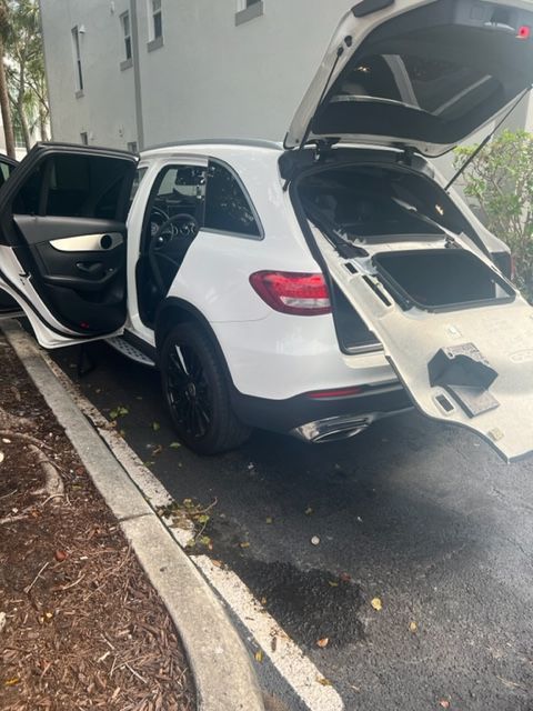 White SUV with open doors and trunk parked beside a curb on a wet street.