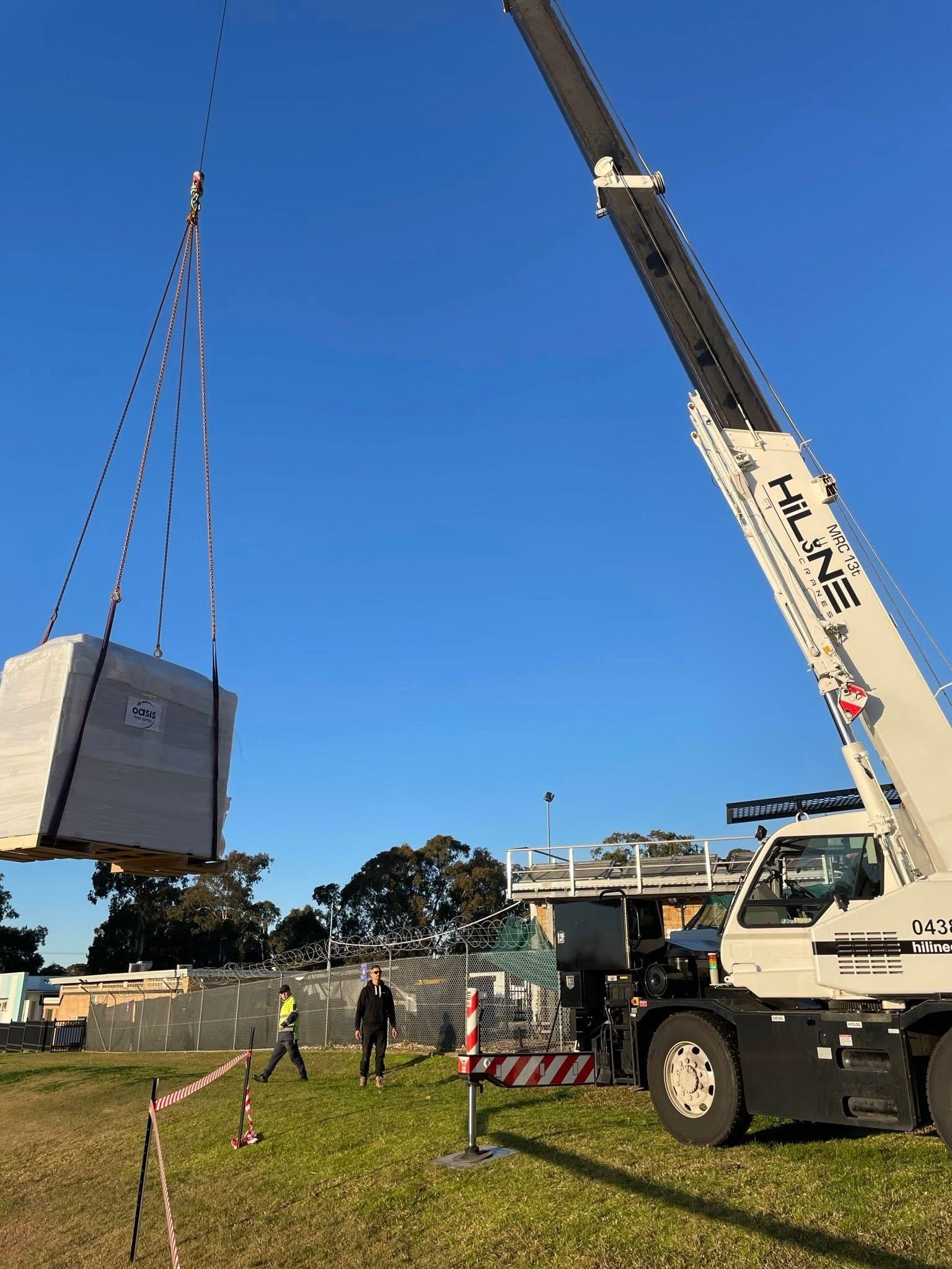 A crane from HiLine Cranes is lifting a large concrete block in a field.