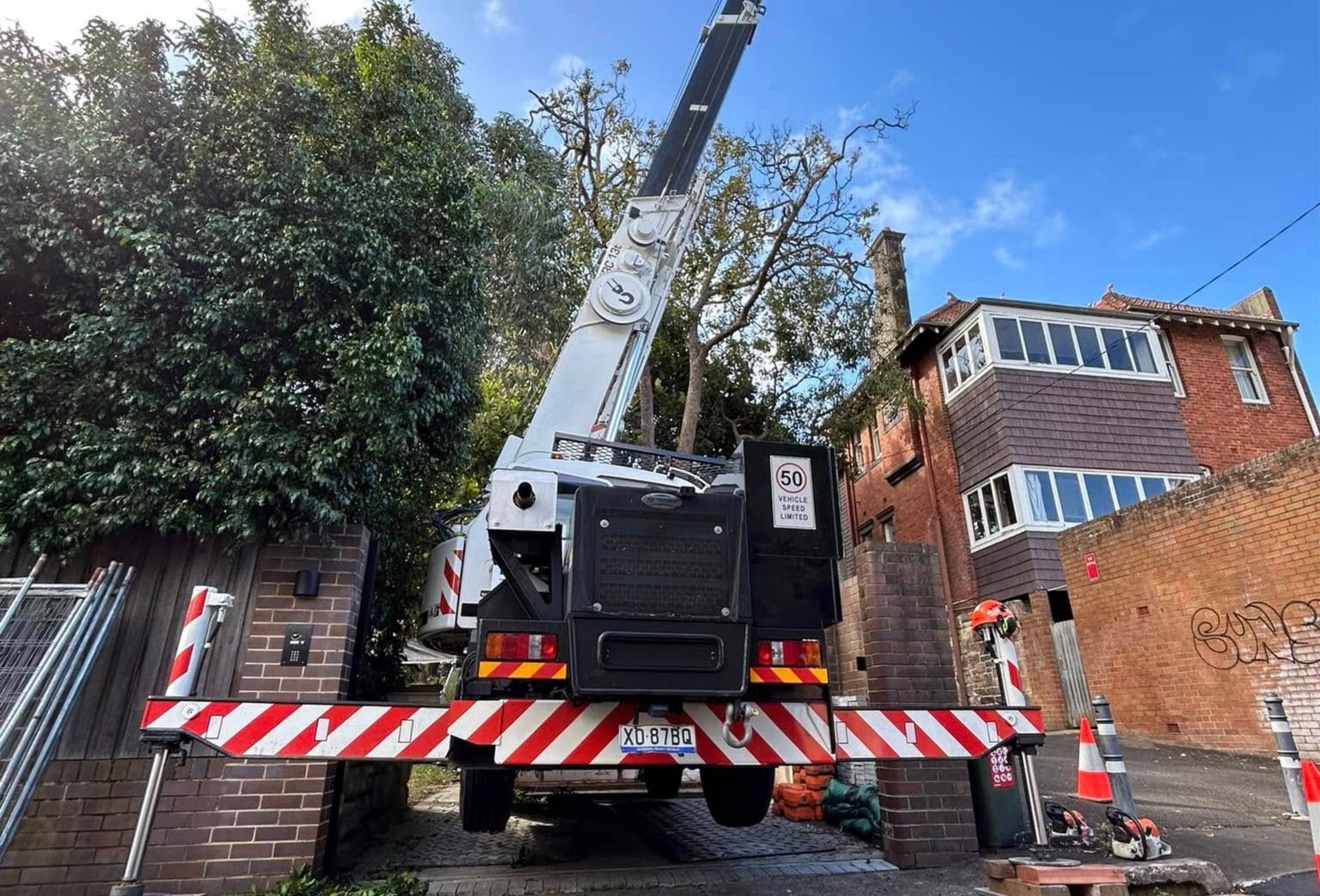 A crane truck trimming a tree near a brick building.