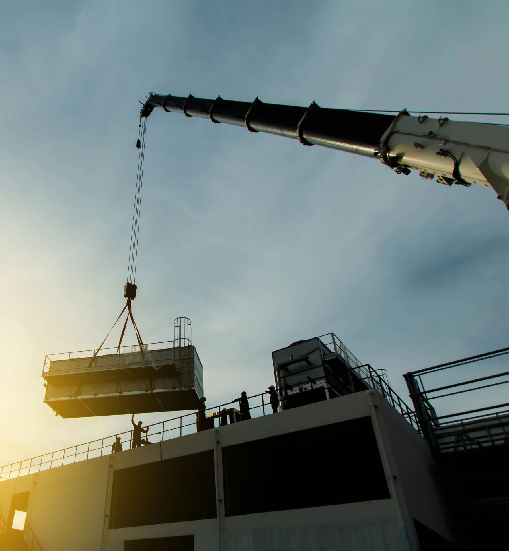 A large crane is lifting a cooling machine on top of a building.