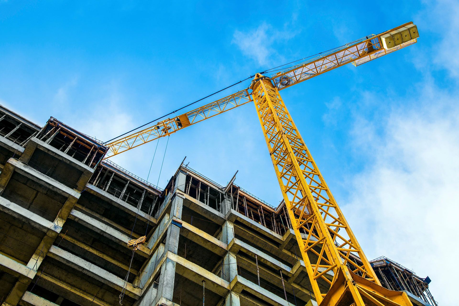 Construction crane lifting materials at a multi-story building against a blue sky.