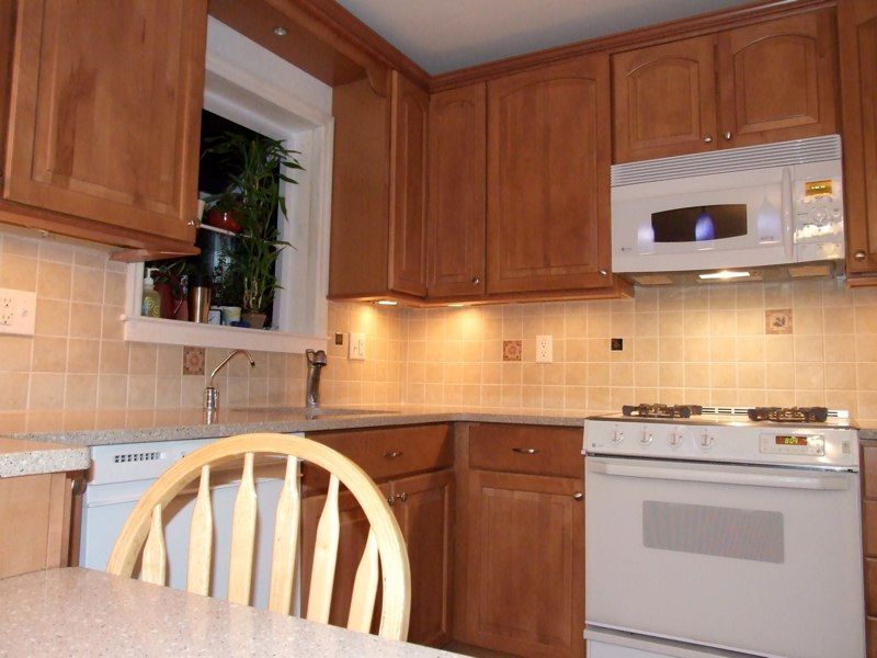 L-shaped kitchen with brown cabinets, blue countertops, and yellow walls. Decorative wine racks hang above the sink.