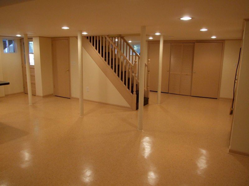 Interior basement with staircase, laundry area, and light wood flooring. White walls, black railing.