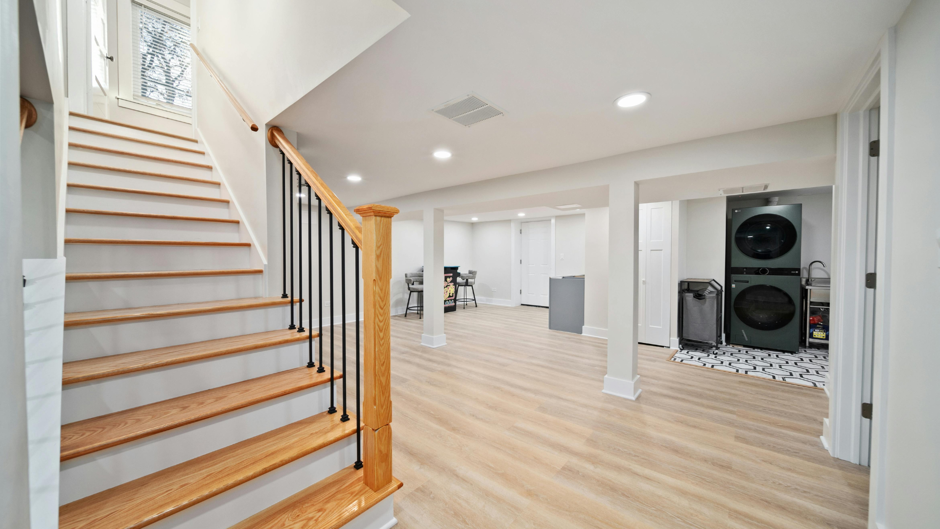 Interior basement with staircase, laundry area, and light wood flooring. White walls, black railing.