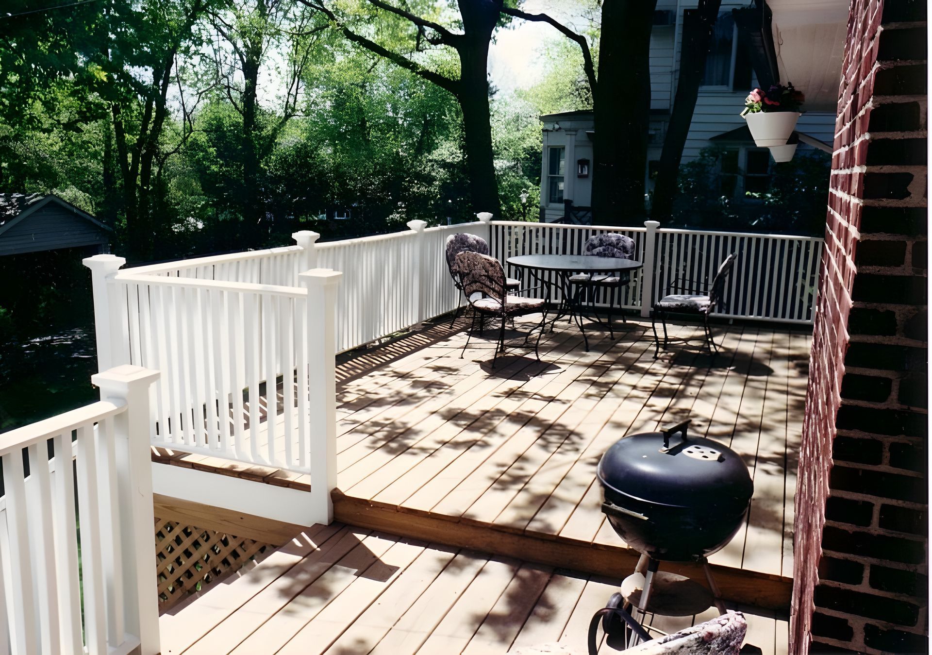 Woven chair on a wooden deck by a pond, with a glass door in the background and lush greenery.