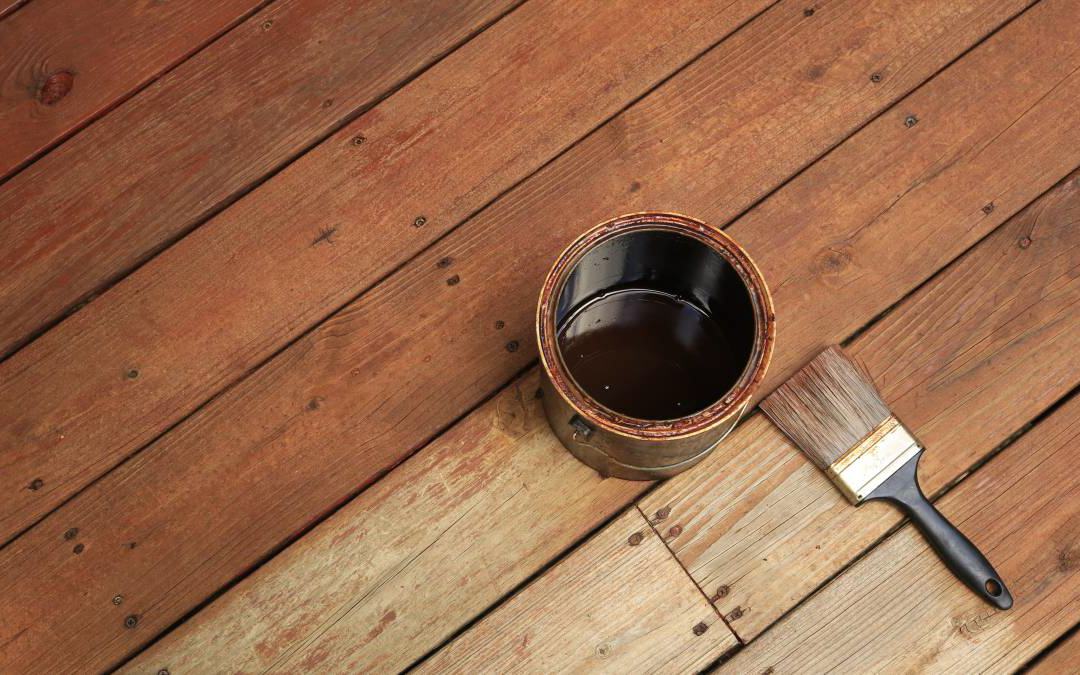 A container of wood stain and a brush on small section of hardwood flooring.