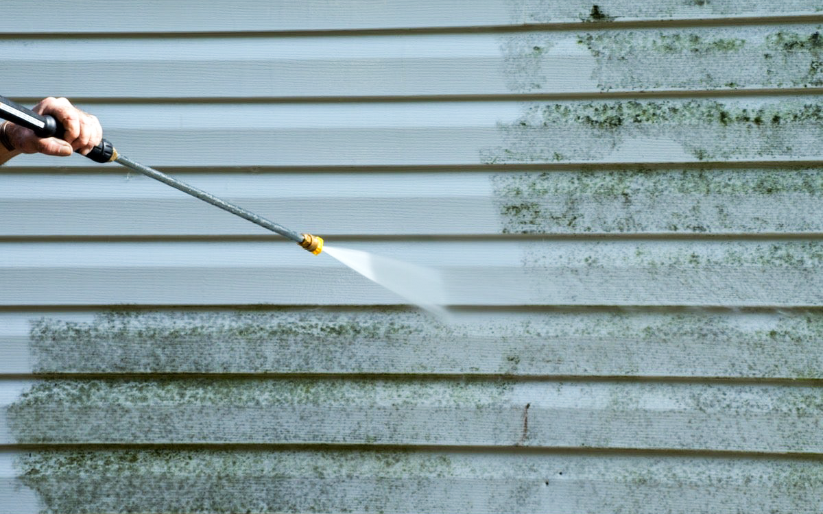 Power washing a wall of dirty siding.