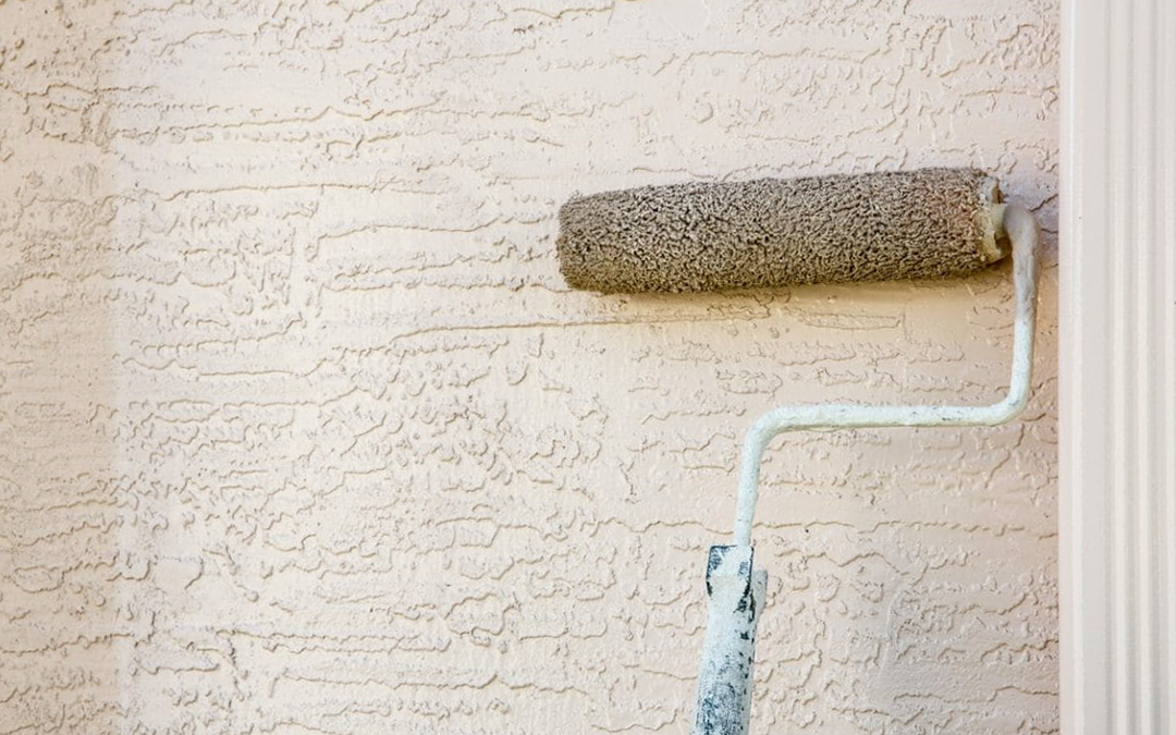 A paint roller in the process of painting a section of stucco.