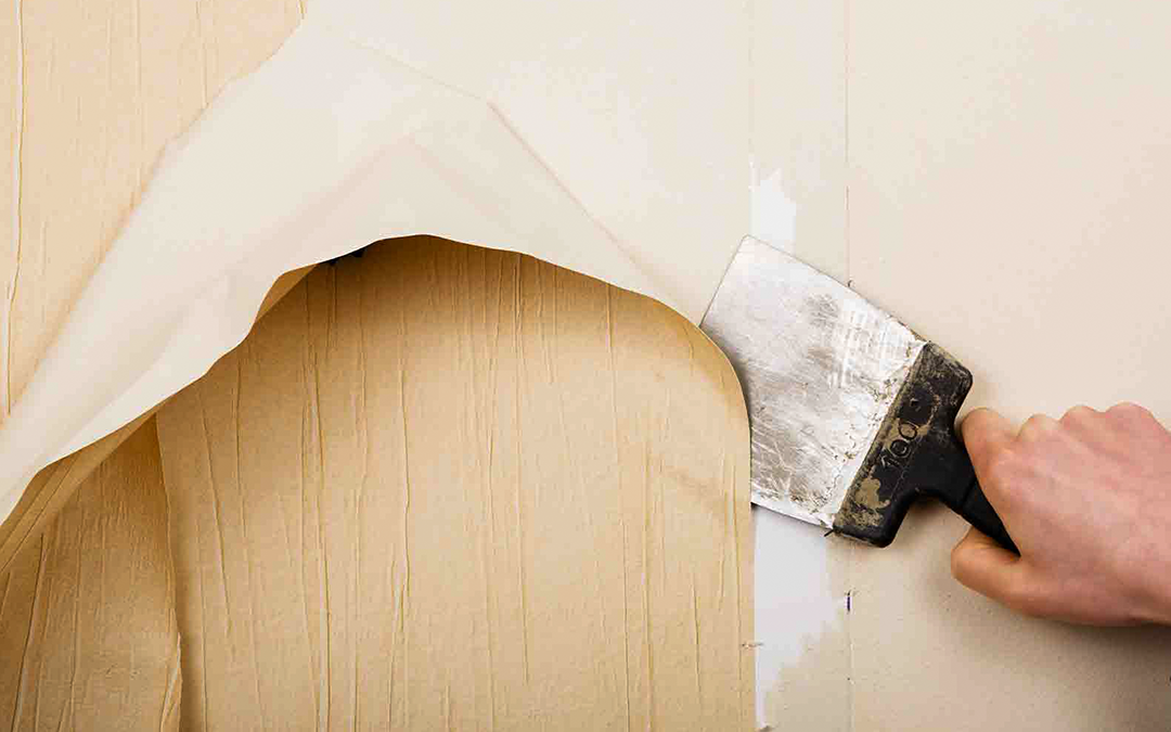 Removing a section of wallpaper from a wall using a hand tool.