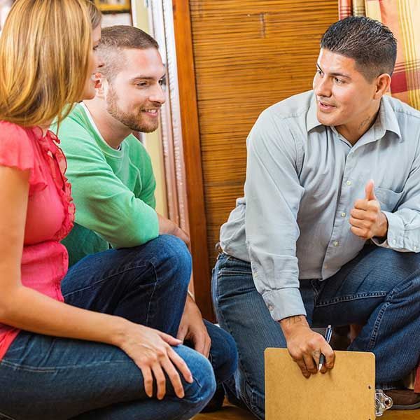 A man is kneeling down with a clipboard and giving a thumbs up