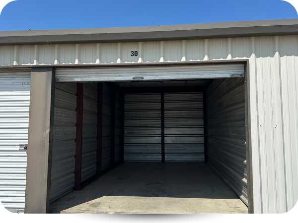 An open, empty self-storage unit with metal walls and a concrete floor under a clear blue sky.