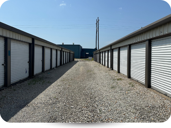 A gravel aisle between two rows of metal roll-up storage units under a clear blue sky.