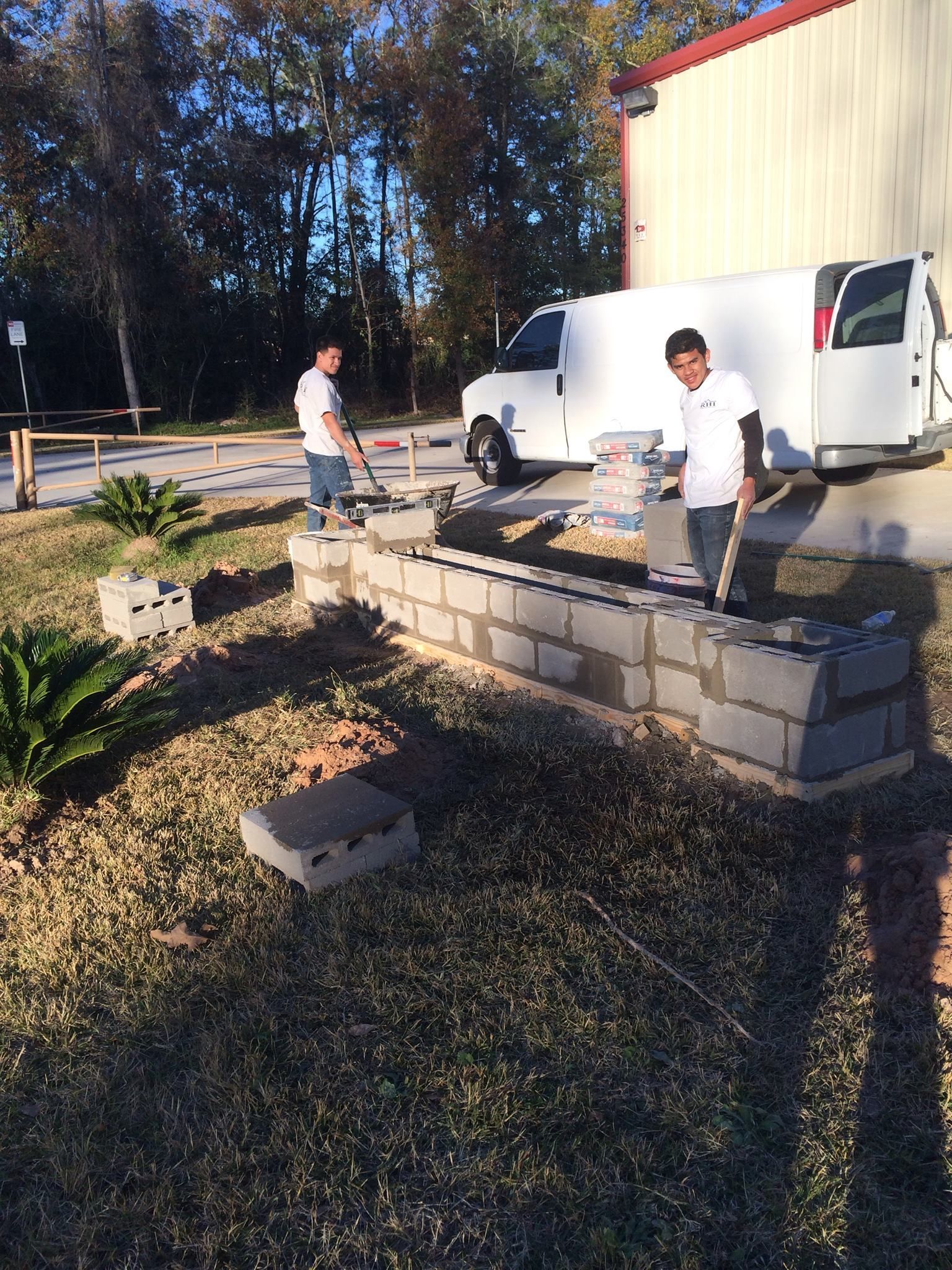 Two men are working on a brick wall in front of a white van.