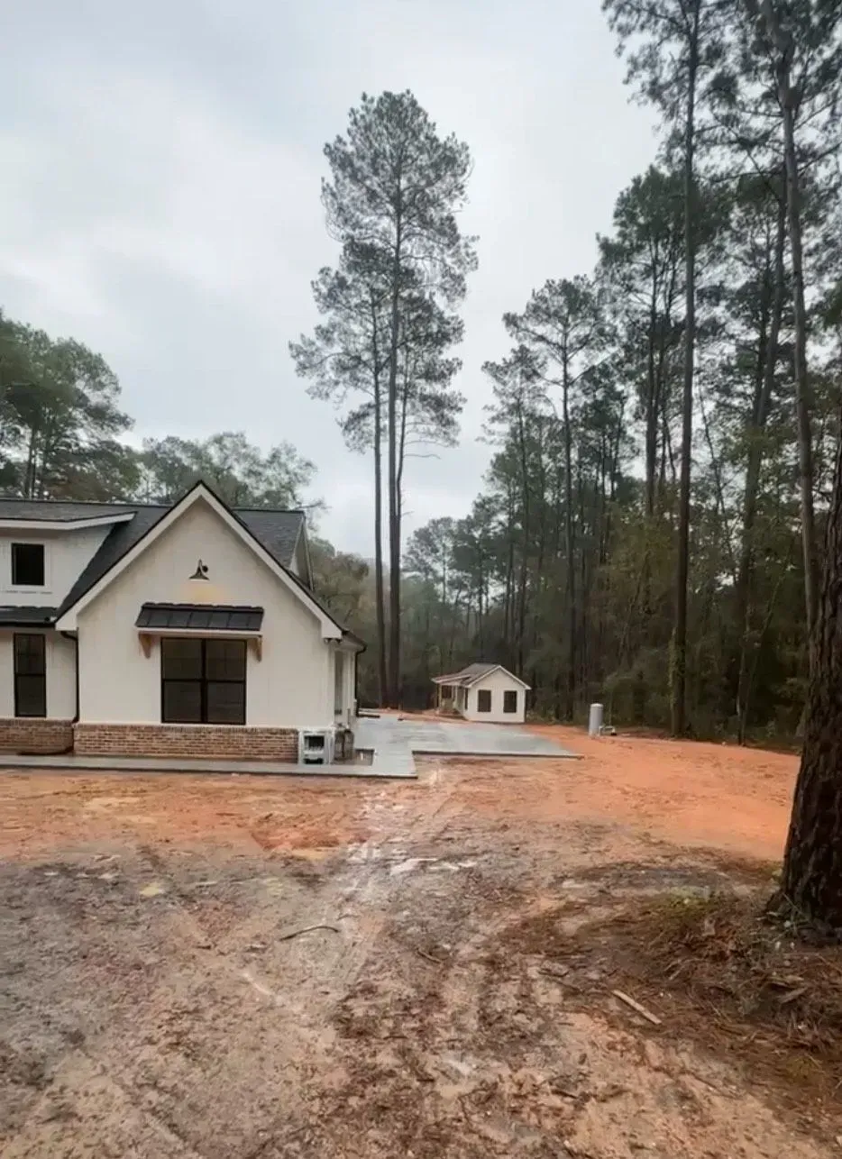 New house construction site in a wooded area; unfinished house with attached garage and detached small building.