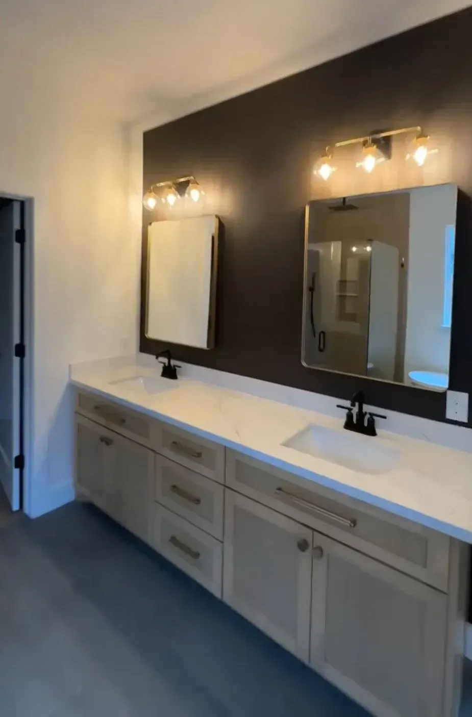 Bathroom with double vanity, light wood cabinets, black fixtures, and a dark accent wall with mirrors and sconces.