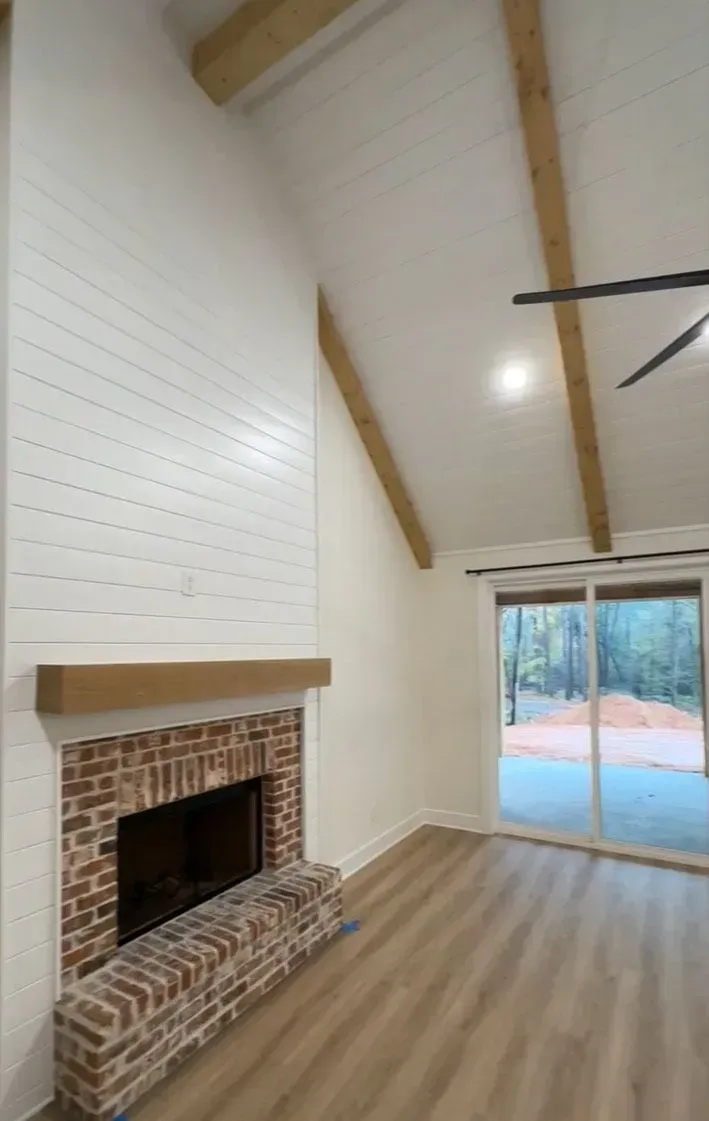 Living room with brick fireplace, white shiplap walls, wooden beams, and sliding glass doors.