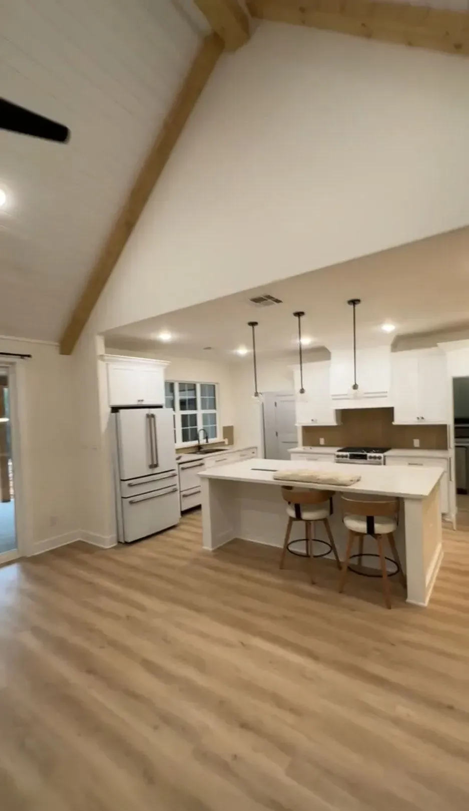 Spacious kitchen with white cabinets, island, and light wood flooring under a vaulted ceiling with a wood beam.