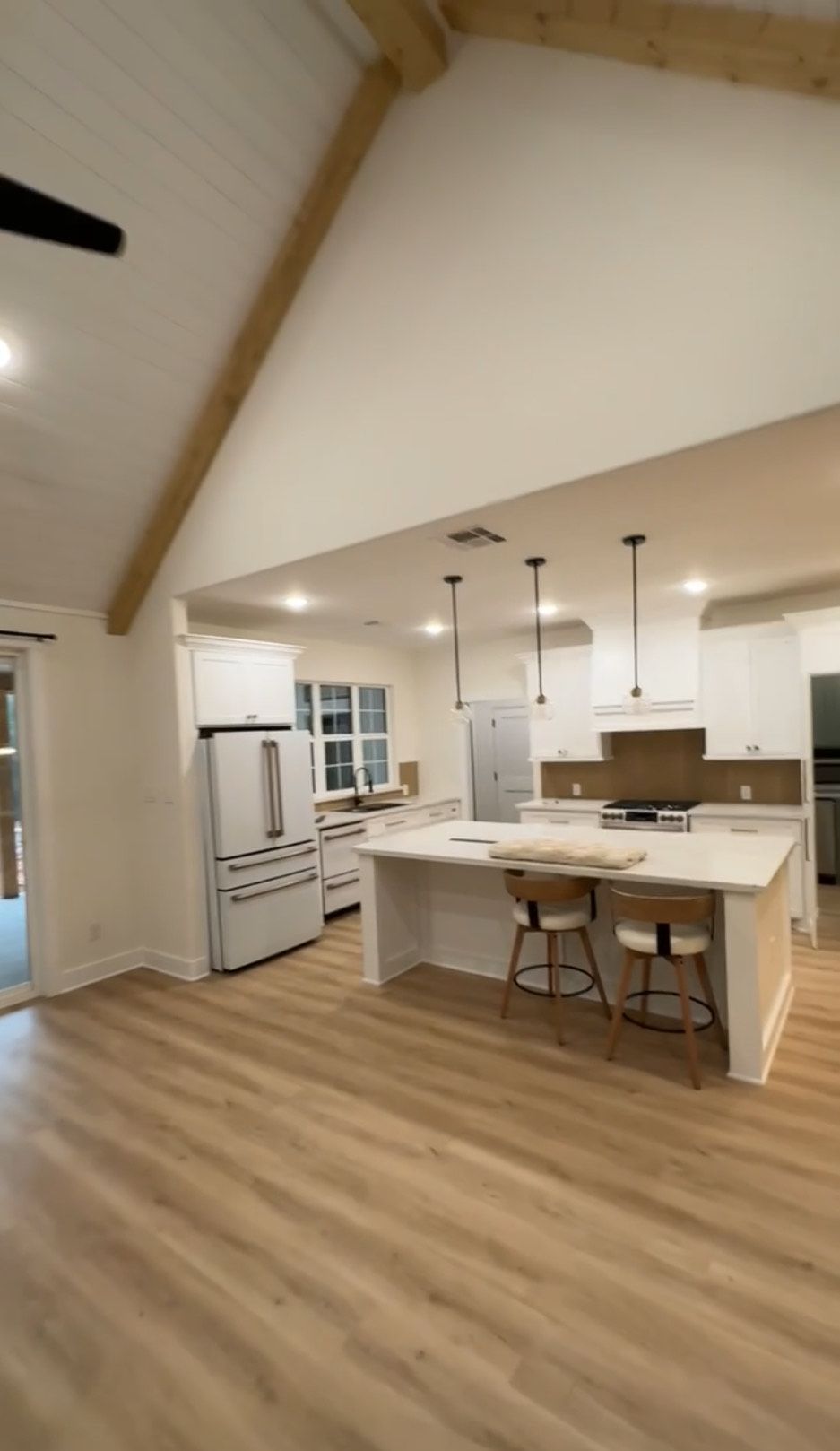 Interior view of a bright kitchen with white cabinets, a large island, and a vaulted ceiling with a wooden beam.