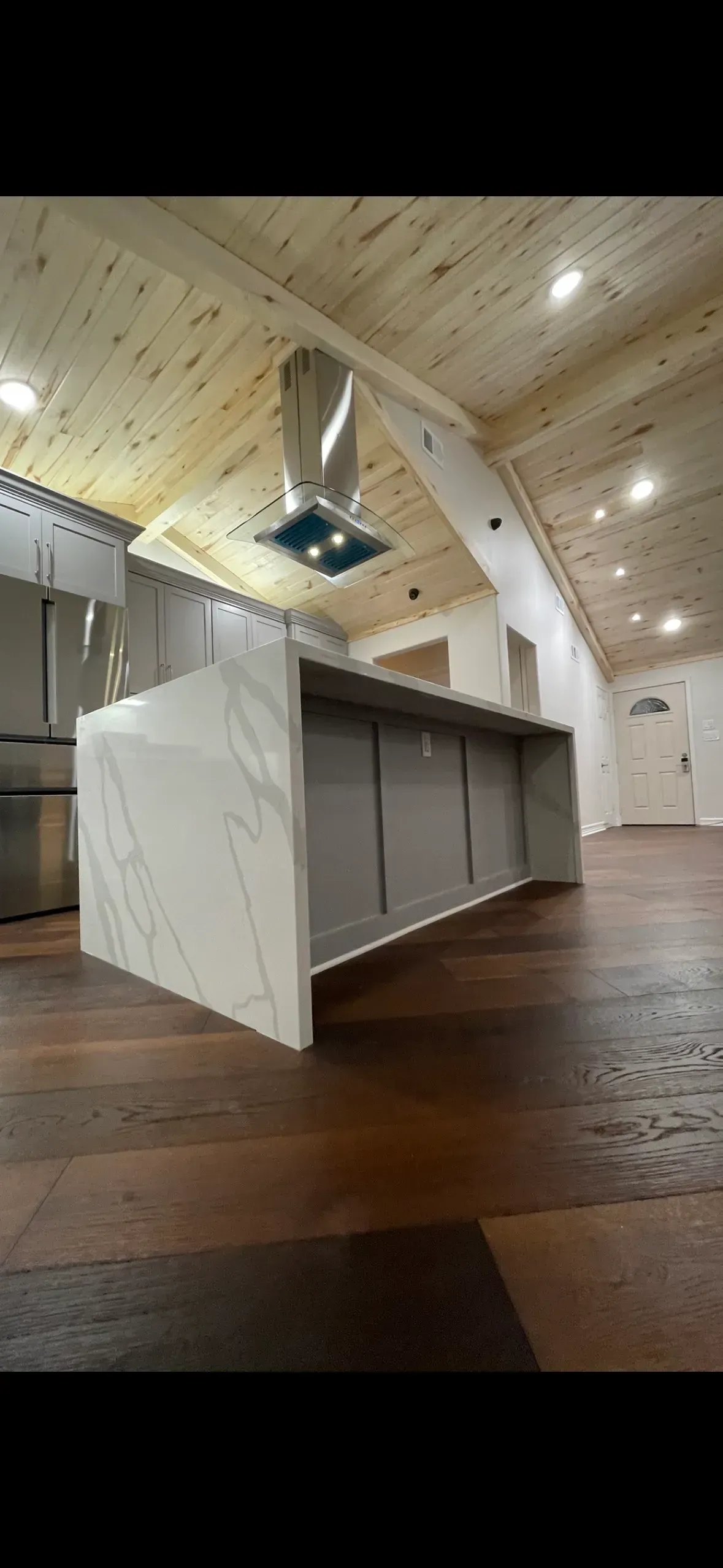 Kitchen with a large island featuring marble-like counter and stainless steel vent hood.