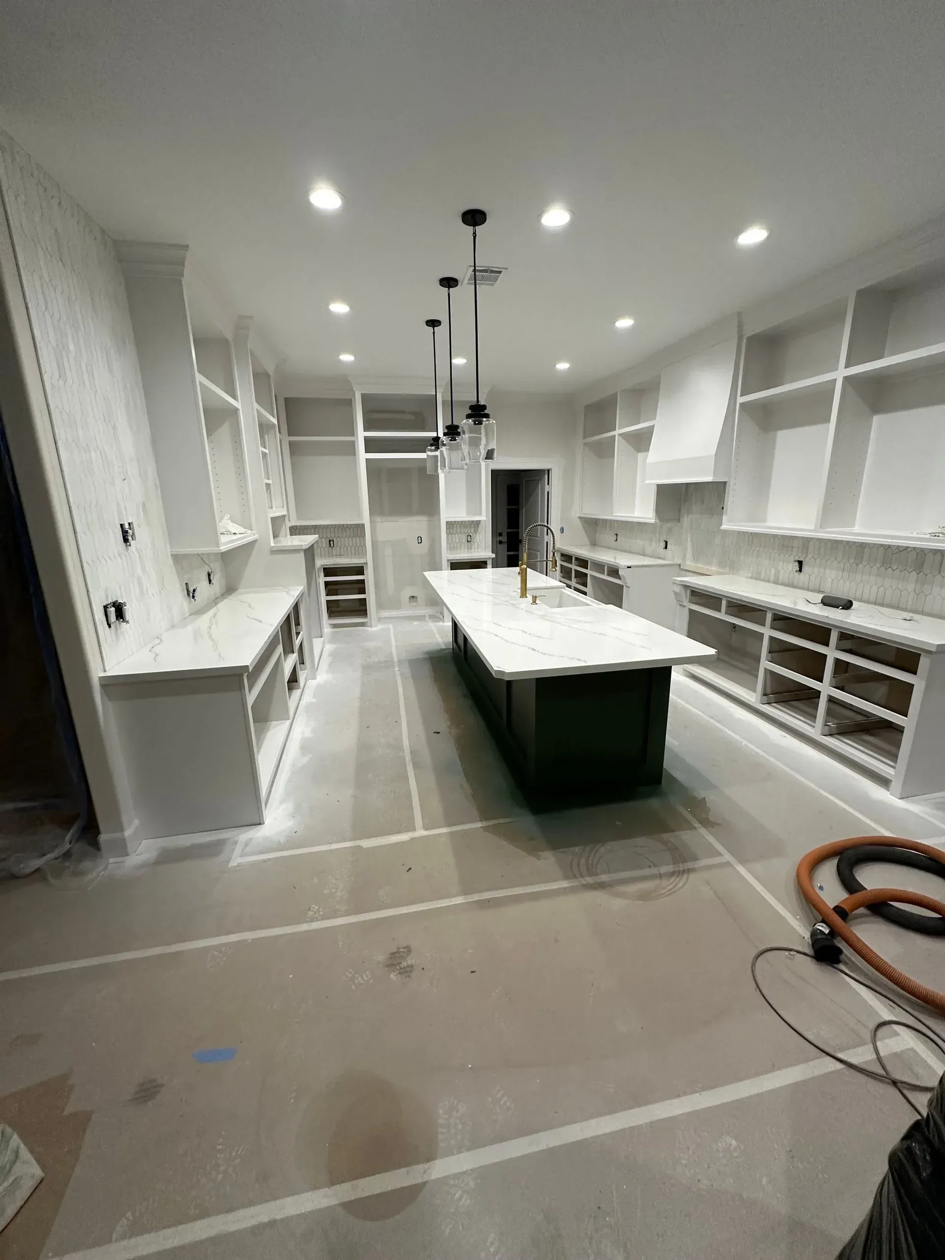 A kitchen under construction with white cabinets, a dark green island, and overhead lighting.