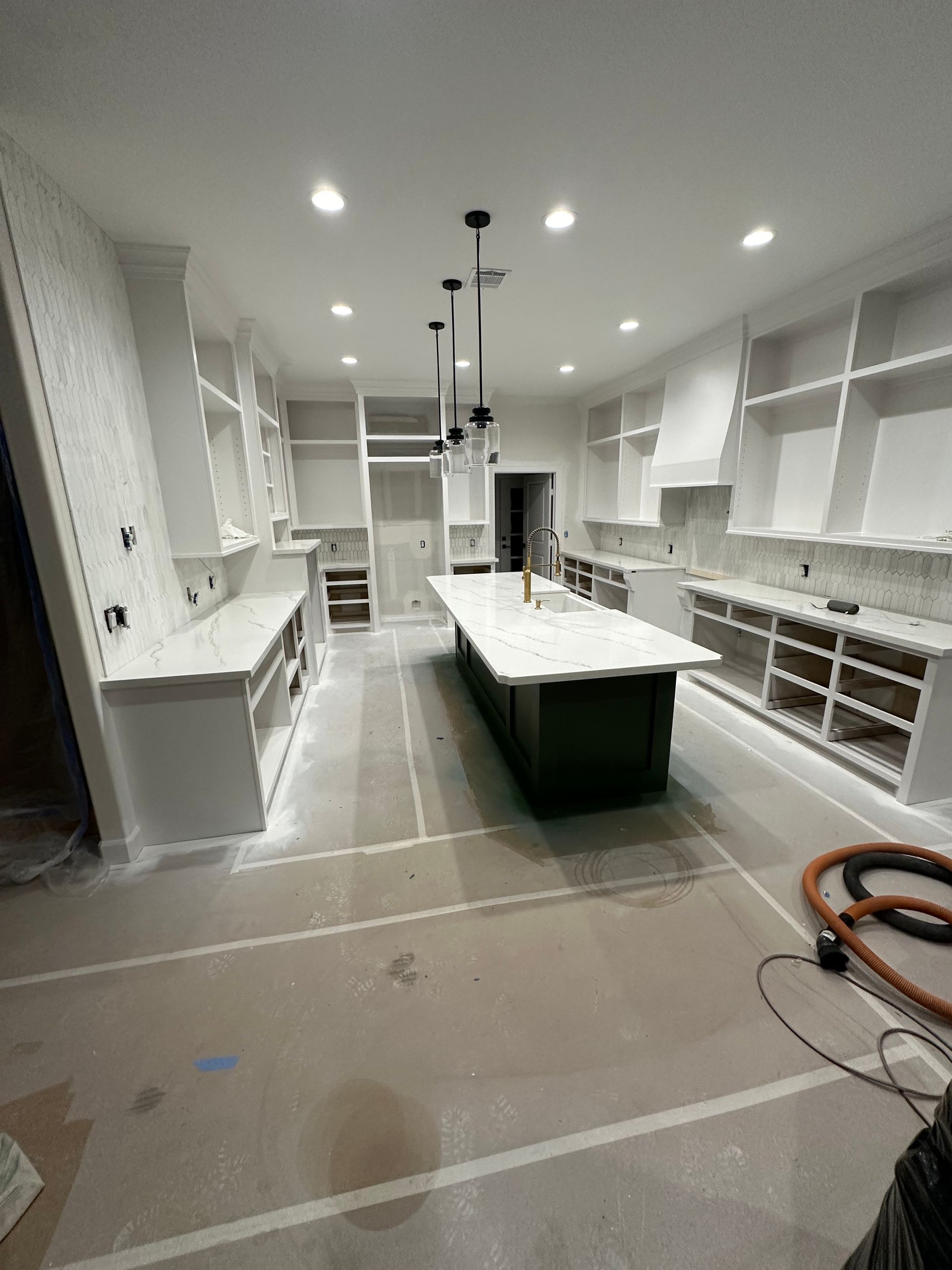 White and green kitchen under construction. Kitchen island with countertop, white cabinets and shelving, overhead lighting.