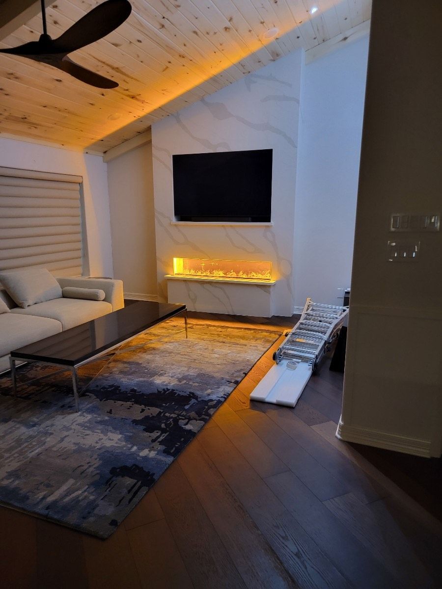 A modern living room with a fireplace, TV, and a low coffee table over a rug. Warm lighting illuminates the space.