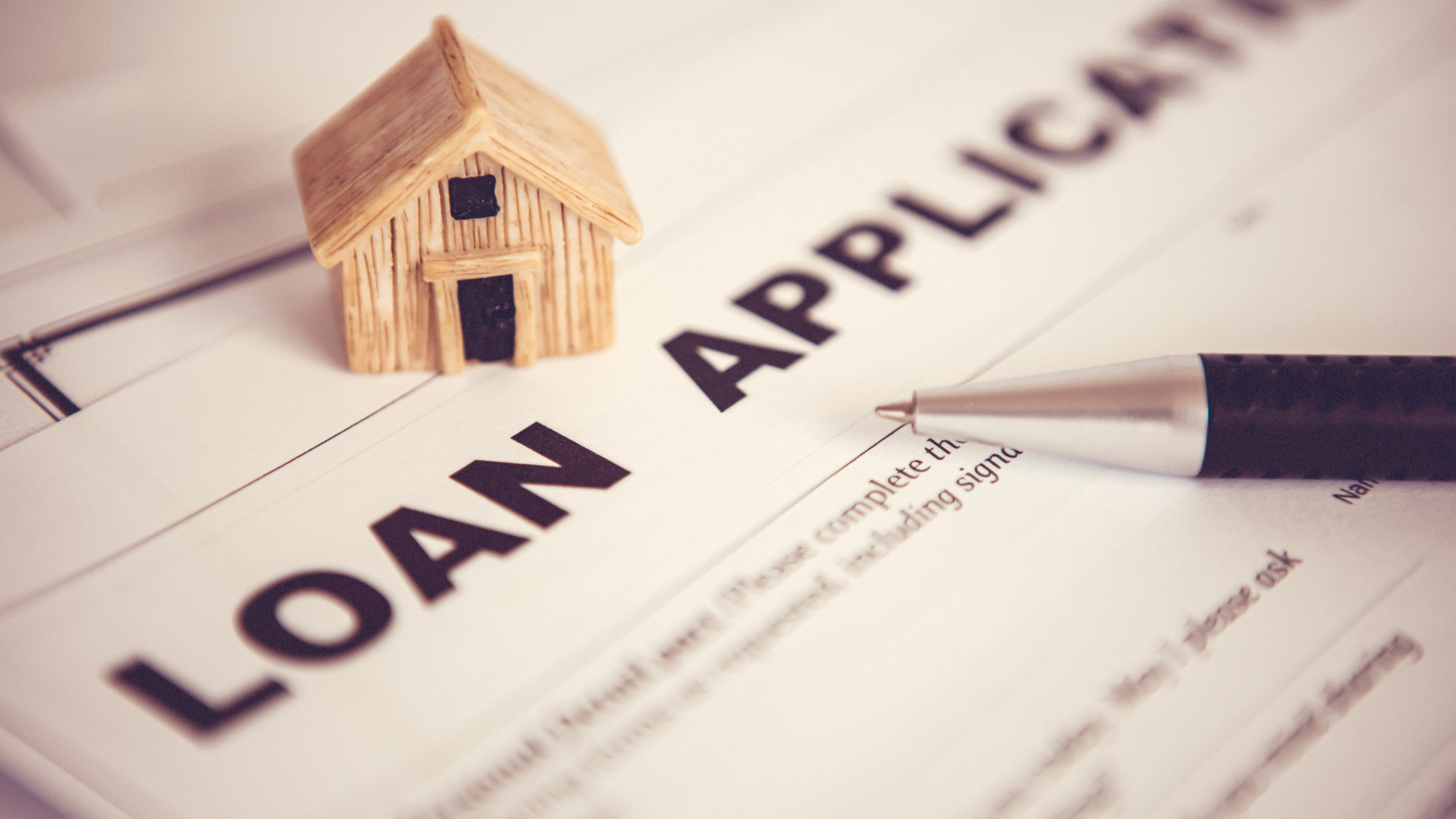A small wooden house is sitting on top of a loan application form.