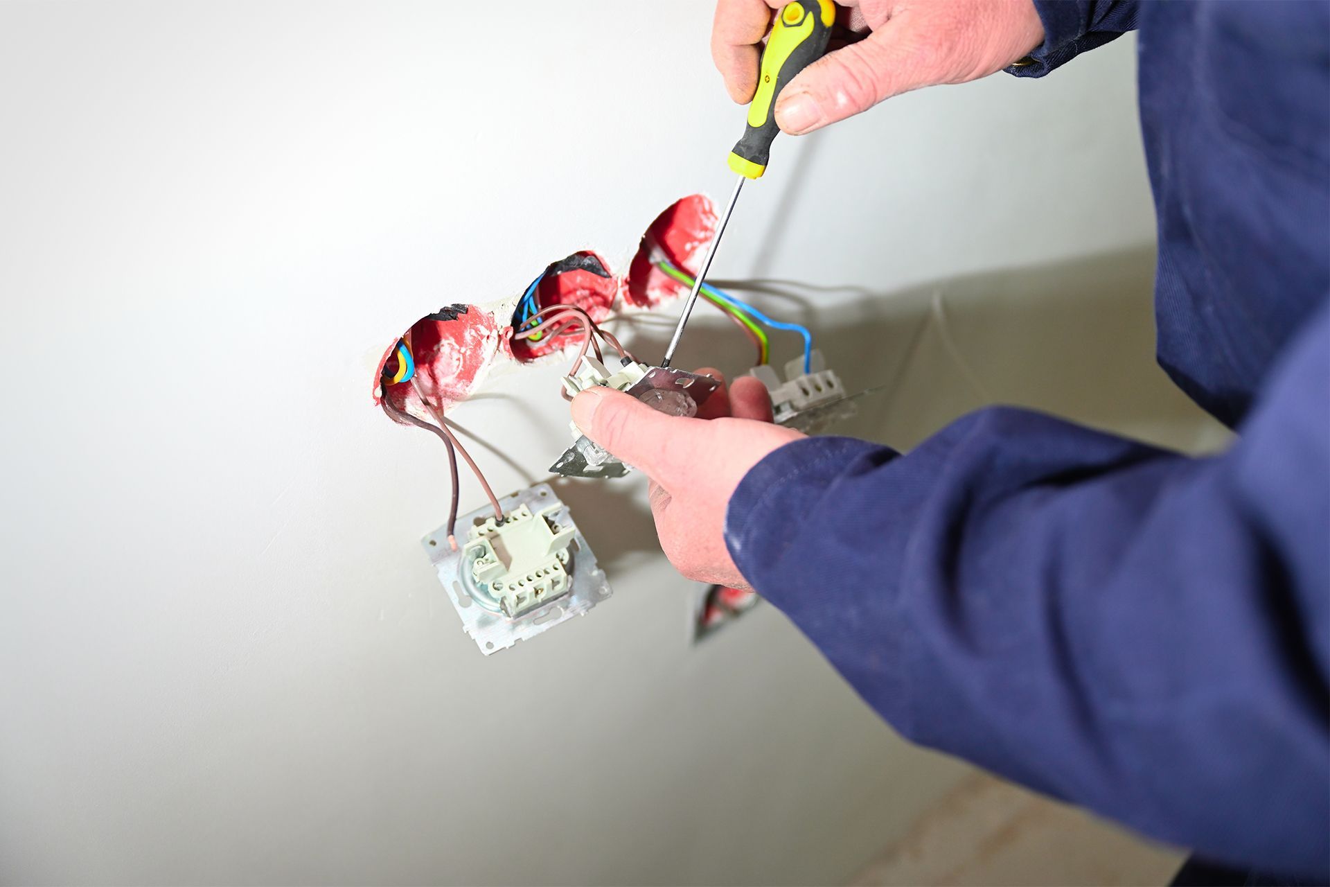 Hands wiring a small circuit with red components on a table using a screwdriver.