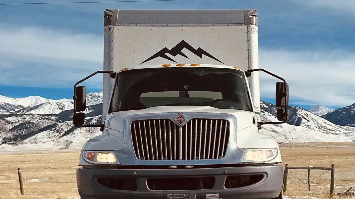 A white truck is parked in a field with mountains in the background.