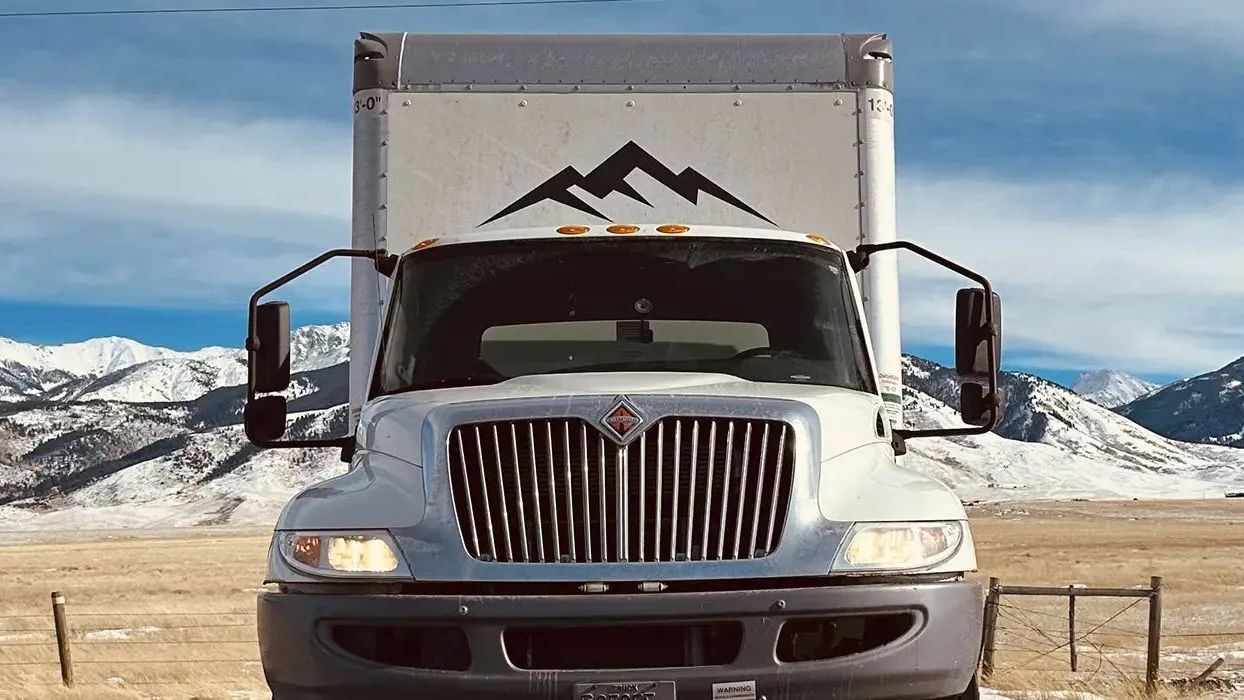 A white truck is parked in a field with mountains in the background.