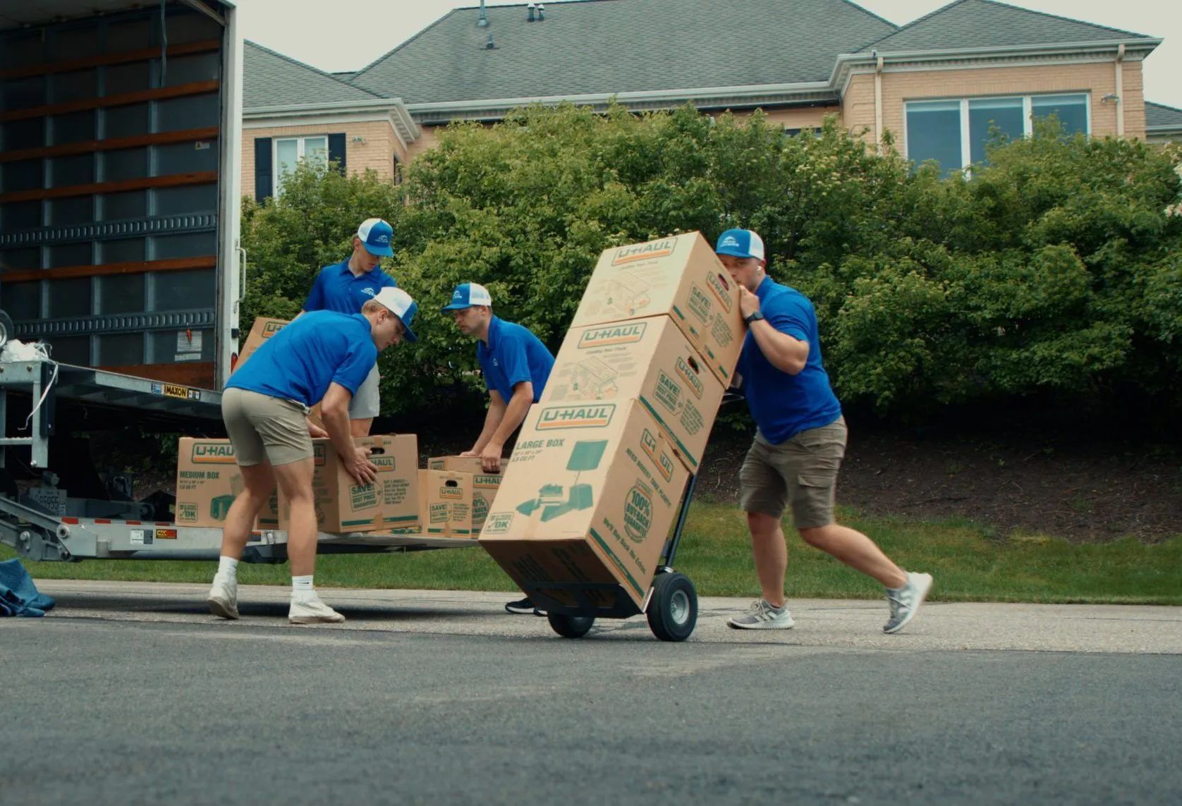 Movers in blue uniforms loading boxes onto a truck outside a house.