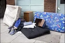 A pile of junk is sitting on the sidewalk in front of a garage.
