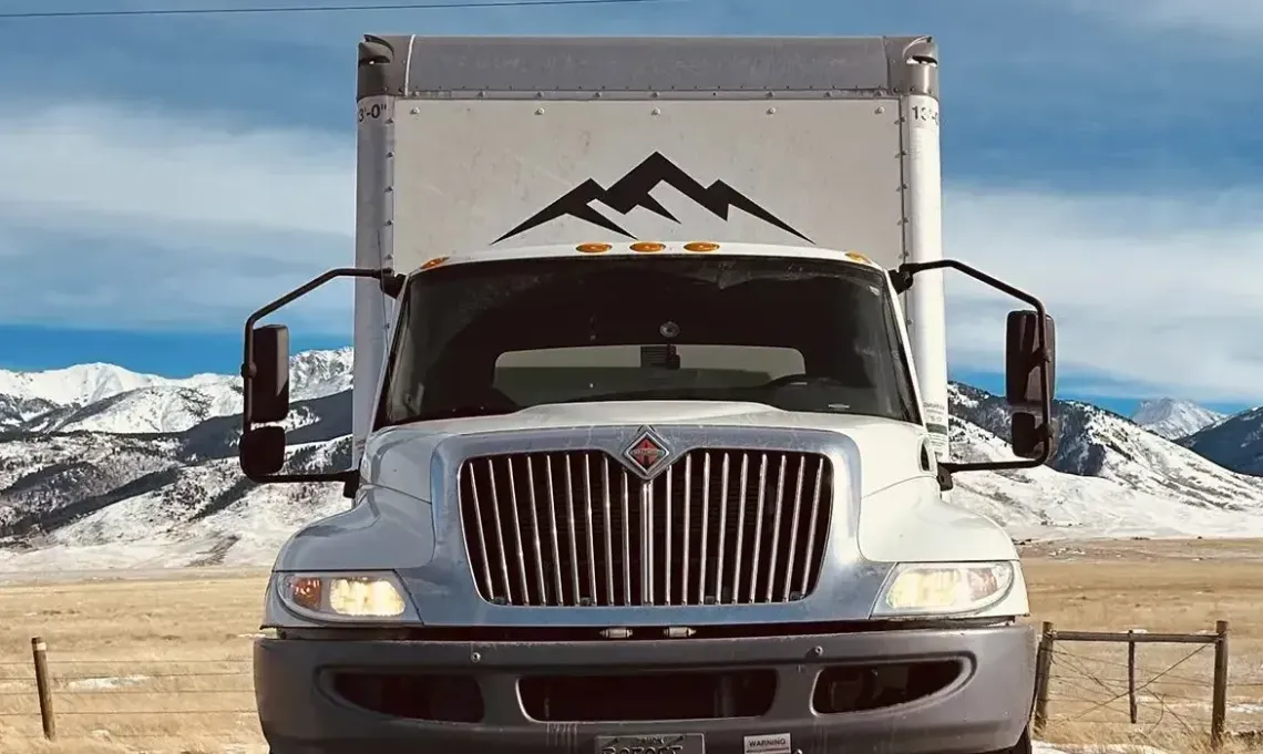 A white truck is parked in a field with mountains in the background.
