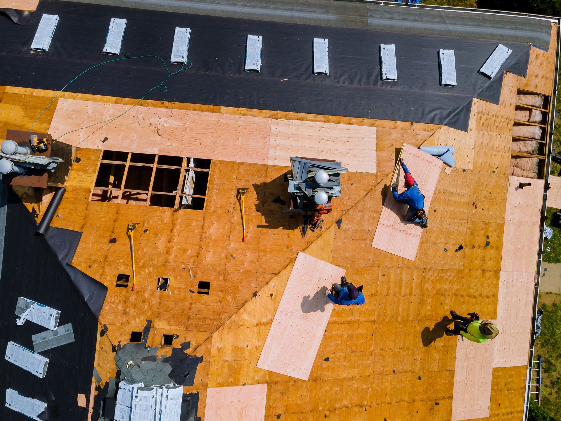 Aerial view of a roof under construction with workers installing new plywood and roofing materials.