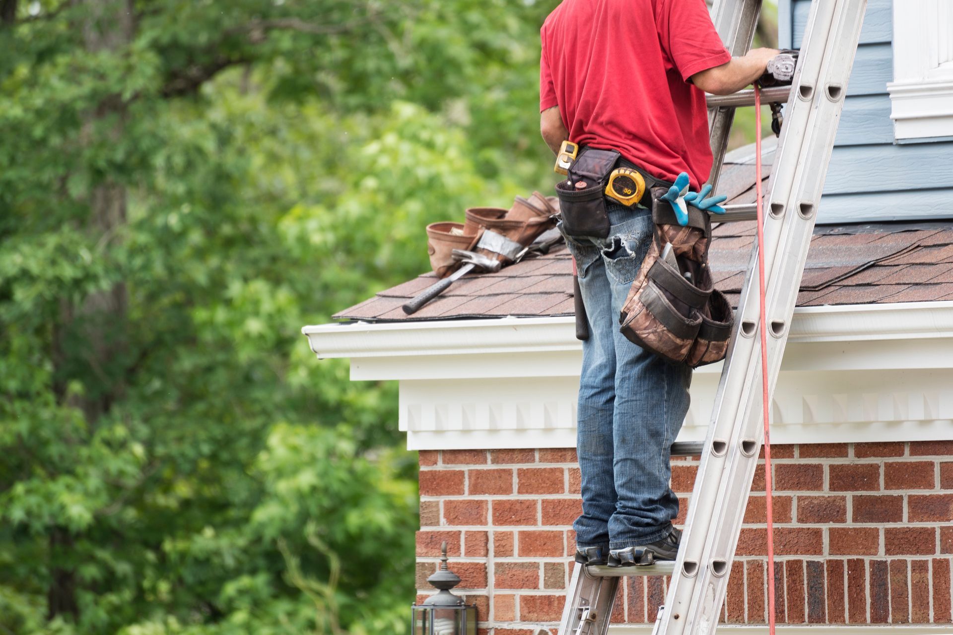 A man is standing on a ladder on the roof of a house.