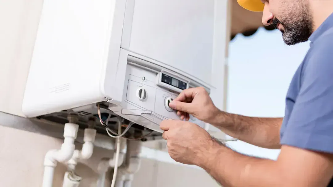 Technician adjusting a wall-mounted boiler with a wrench.