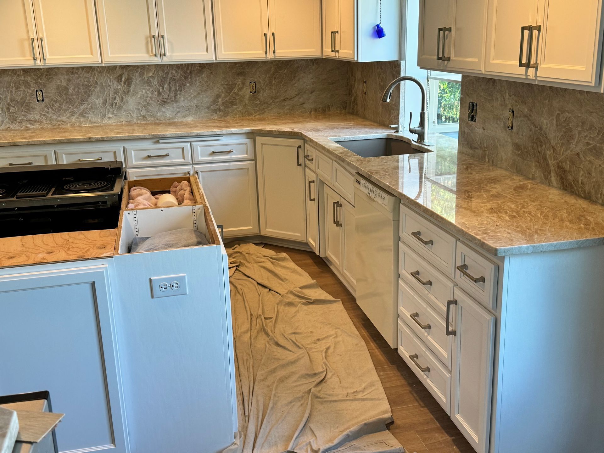 Kitchen under renovation with white cabinets, open dishwasher, and protective floor covering