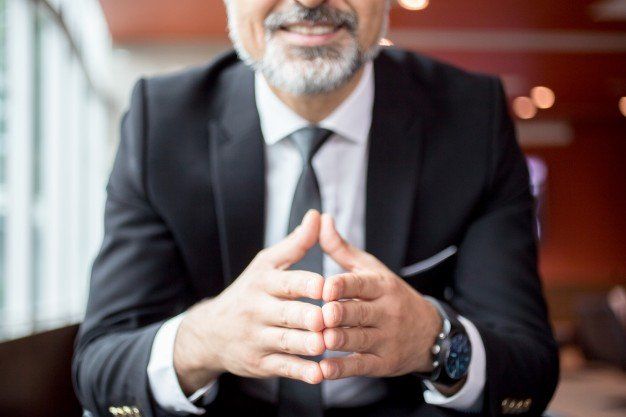 Man in suit with hands clasped, smiling, indoors.