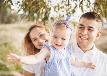 Family with baby, outdoors; parents smiling, baby with arms out.