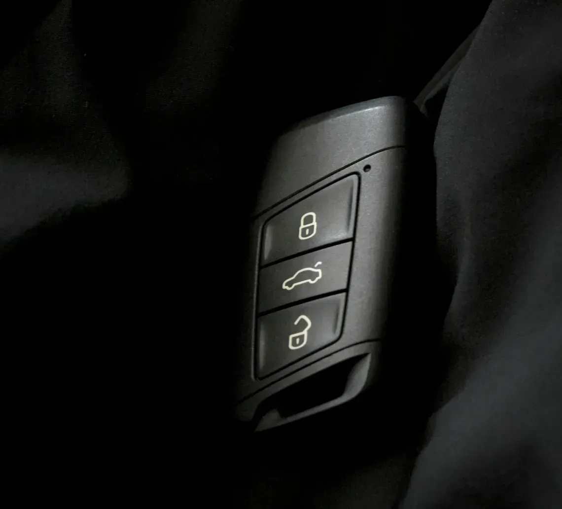 A black car key fob with three function buttons rests against a dark, textured fabric background.