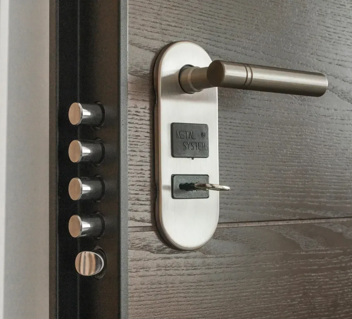 A close-up of a modern wooden door with a metallic handle, a key inserted in the lock, and four extended deadbolts.
