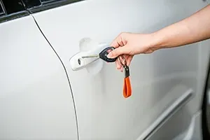 A person's hand inserts a car key with an orange strap into the handle of a white vehicle.