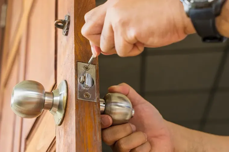 A person uses a screwdriver to install or repair a silver doorknob on a wooden door.