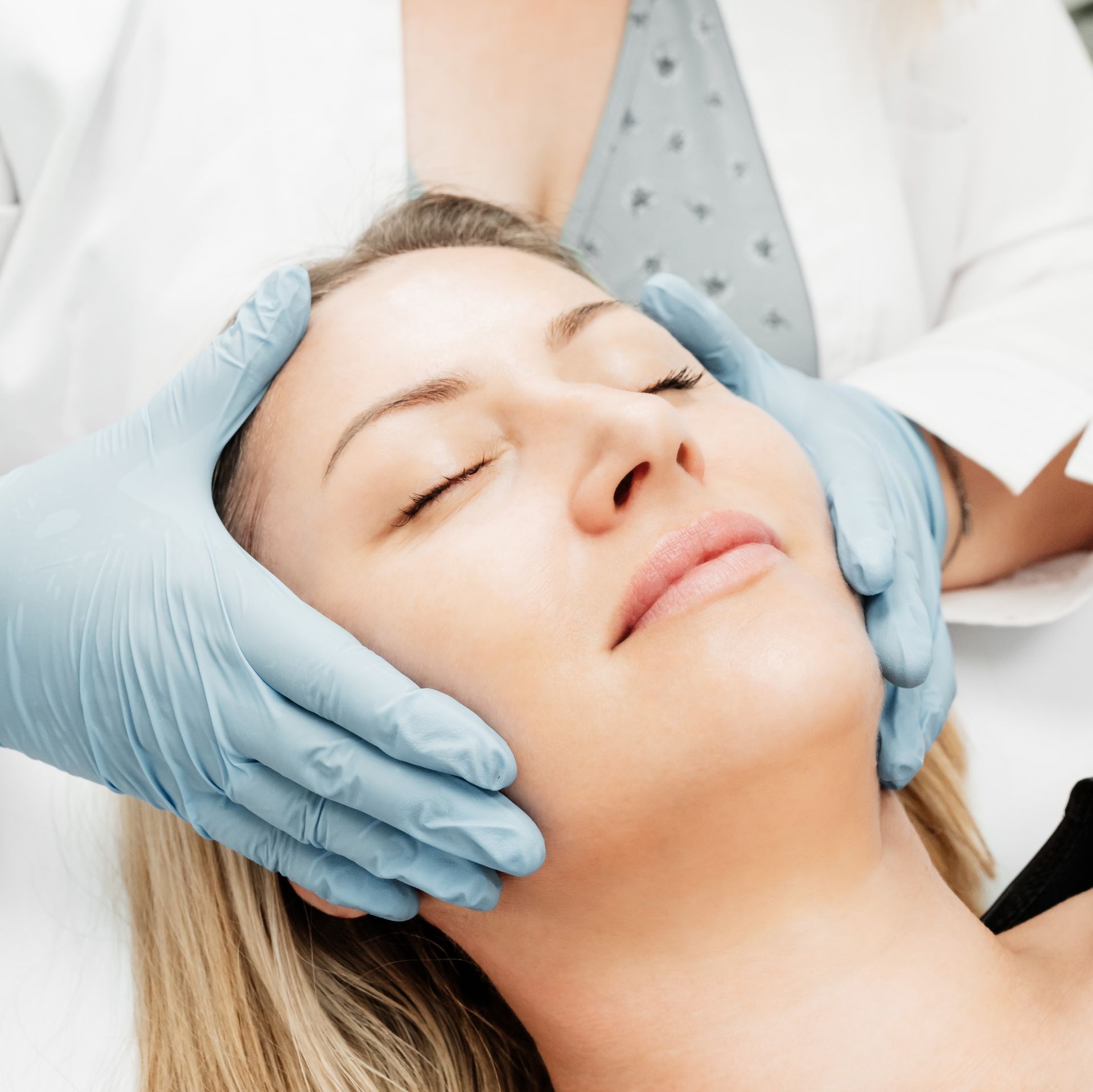 A woman is getting her face examined by a doctor wearing blue gloves