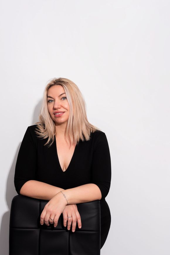 a woman in a black dress is sitting on a black chair against a white wall .